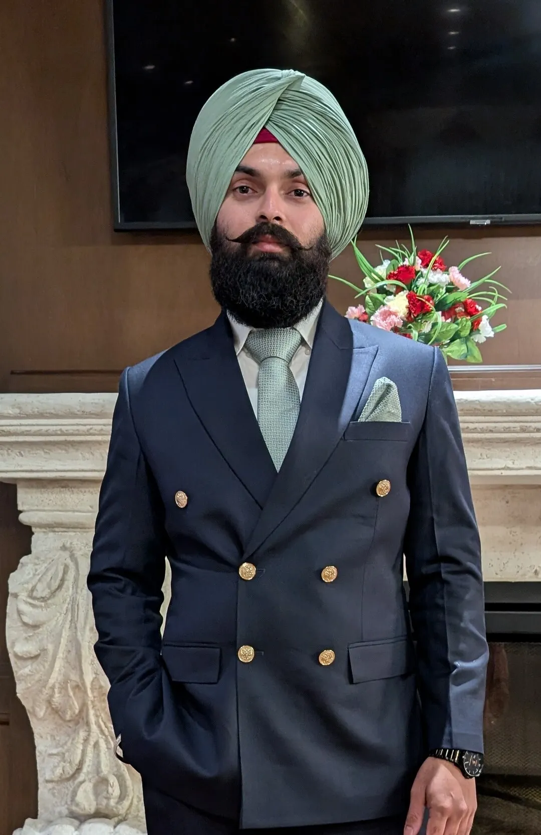 Gurkanwaljot Singh Brar in a navy double-breasted suit with gold buttons and a sage-green turban
